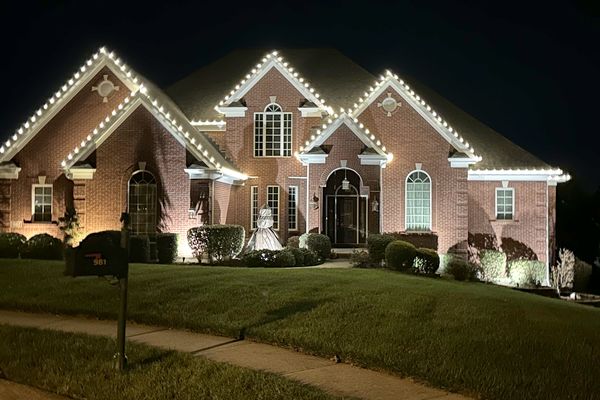 Brick home with warm white C9 Christmas lights outlining every roofline peak at night